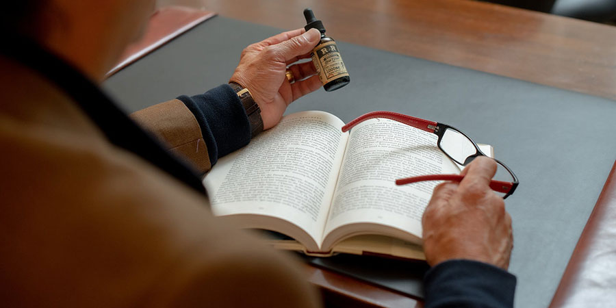a person holding a bottle of hemp extract and an eyeglass while sitting in front of an office desk with a book on top of it